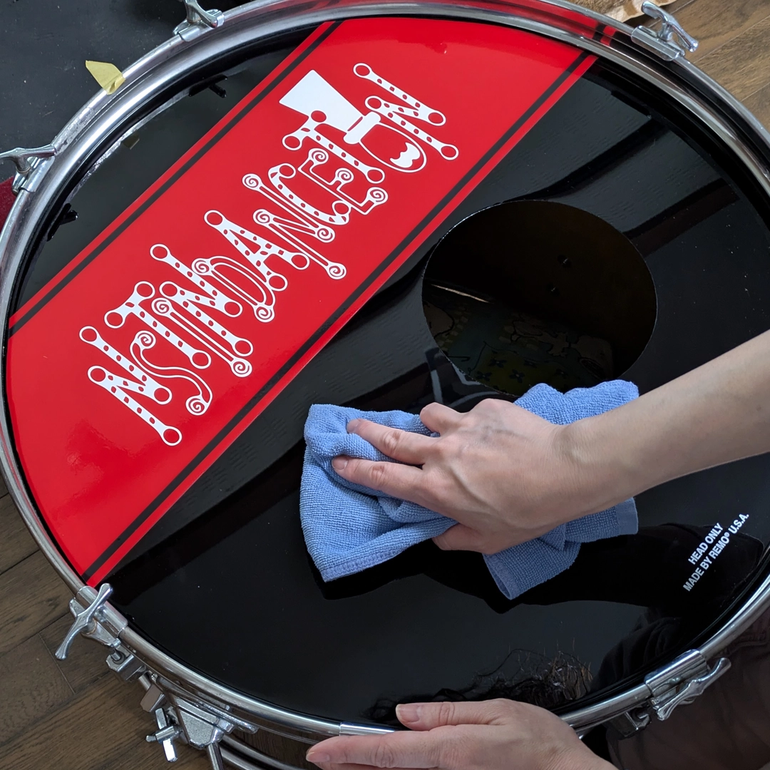 バスドラムヘッドにステッカーを貼る前に、ヘッドの汚れを落としている